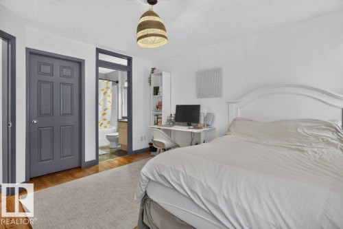 Bedroom featuring hardwood-style flooring, a recessed six-panel door, and a partially visible bathroom with a tub and single vanity - 21320 90 Avenue, Edmonton, AB 