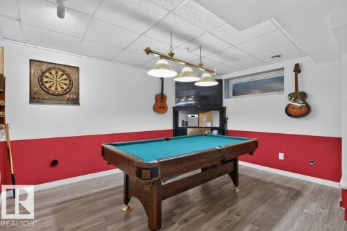 Recreation room featuring a pool table with a brass light fixture, wood-finish flooring, a horizontal window, and a drop ceiling - 21320 90 Avenue, Edmonton, AB 