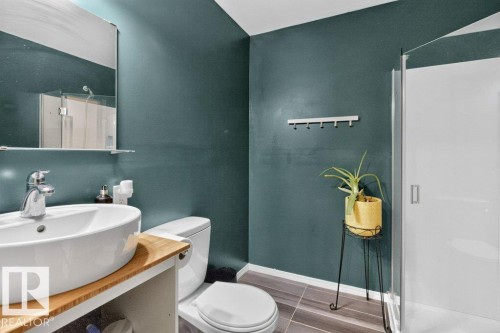 Bathroom featuring a vessel sink with a chrome faucet, wood-finish countertop, dark teal walls, and a glass-enclosed shower - 21320 90 Avenue, Edmonton, AB 