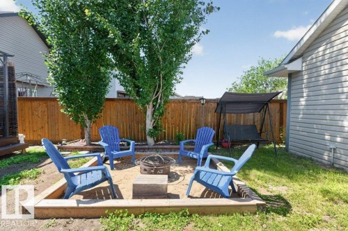 Outdoor fire pit area with timber-framed sand base, surrounded by mature trees and a wood privacy fence - 21320 90 Avenue, Edmonton, AB 
