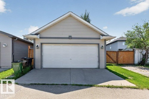 Detached garage with light-toned siding and a white sectional door, featuring concrete driveway and exterior lighting fixtures - 21320 90 Avenue, Edmonton, AB 