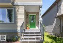 Inviting front entrance featuring a vibrant green door, durable siding, a covered porch, and a window with grid detailing - 21320 90 Avenue, Edmonton, AB 