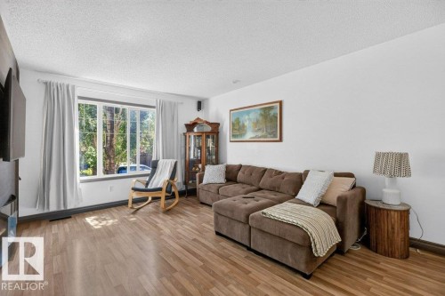 Bright living area featuring wood-finish flooring, a large multi-pane window, white walls, dark trim, and a built-in display cabinet with glass doors - 21320 90 Avenue, Edmonton, AB 