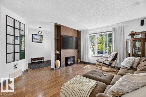 Living area featuring wood-finish flooring, a built-in media center with shelving, an electric fireplace, and a large multi-pane window - 21320 90 Avenue, Edmonton, AB 