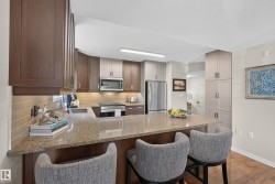 Kitchen featuring a breakfast bar with stone-finish countertops, stainless steel appliances, two-tone cabinetry, and wood-finish flooring - 