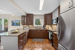 Kitchen featuring wood-finish flooring, dark wood cabinetry, granite-style countertops, stainless steel appliances, and a tiled backsplash - 