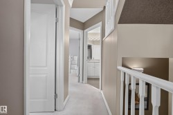 Carpeted hallway featuring a white spindle railing, recessed lighting, and white paneled doors, with a partial view of a bathroom vanity - 