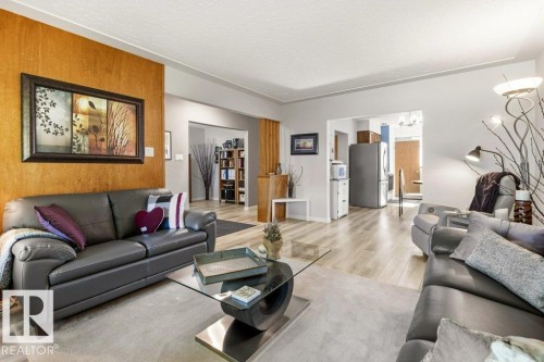 Spacious living area featuring light wood-finish flooring, a textured accent wall, and recessed entryways - 10235 74 Street, Edmonton, AB 