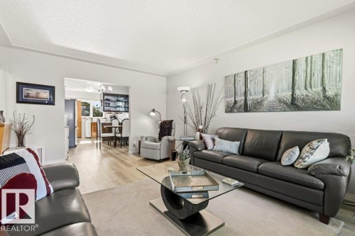 Living area featuring light wood-finish flooring, a neutral wall color, and an open doorway leading to a dining space - 10235 74 Street, Edmonton, AB 