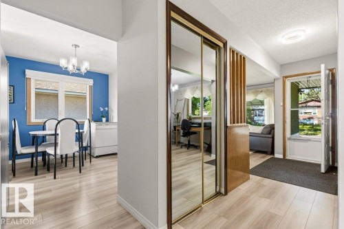 Open-concept interior featuring wood-finish flooring, a dining area with a modern chandelier, and a mirrored closet - 10235 74 Street, Edmonton, AB 