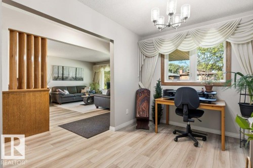 Light wood-finish flooring extends throughout this space, featuring a window with natural light and a contemporary five-light chandelier - 10235 74 Street, Edmonton, AB 
