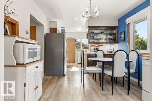 Kitchen area featuring wood-finish flooring, a contemporary chandelier, and a large window with blue accent wall - 10235 74 Street, Edmonton, AB 