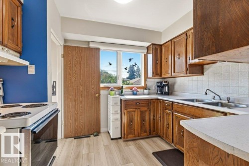 Kitchen featuring light wood-finish flooring, white countertops, wood cabinetry, a tile backsplash, and a double basin sink - 10235 74 Street, Edmonton, AB 