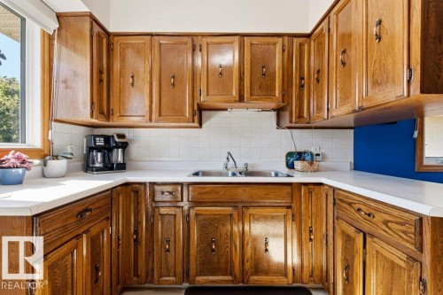U-shaped kitchen with wood-finish cabinetry, white countertops, a double basin stainless steel sink, and white tile backsplash - 10235 74 Street, Edmonton, AB 