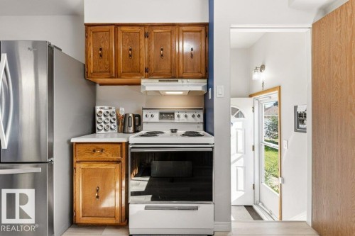 Kitchen area featuring wood cabinetry, white countertops, a white electric range with an overhead vent, and a stainless steel refrigerator - 10235 74 Street, Edmonton, AB 
