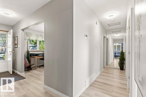 Bright entryway featuring wood-finish flooring extending into a long hallway, with a wide archway opening into a naturally lit area - 10235 74 Street, Edmonton, AB 