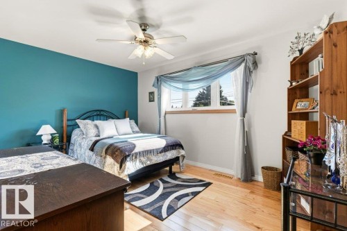 Bedroom featuring a vibrant accent wall, light wood-finish flooring, a ceiling fan with integrated lighting, a window with natural light, and a built-in wooden shelving unit - 10235 74 Street, Edmonton, AB 