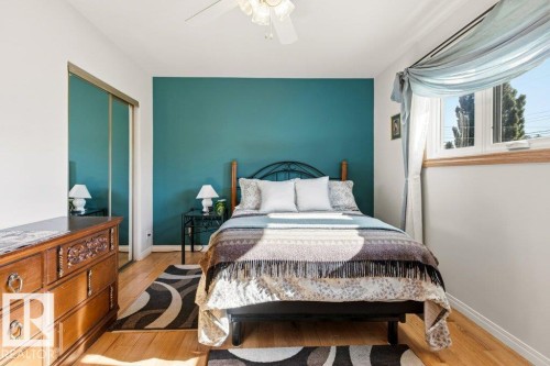 Bedroom featuring wood-finish flooring, a full-lite window, a mirrored closet, a ceiling fan, and a teal accent wall - 10235 74 Street, Edmonton, AB 
