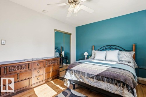 Bedroom featuring a vibrant accent wall, wood-finish flooring, mirrored closet doors, and a ceiling fan with integrated lighting - 10235 74 Street, Edmonton, AB 
