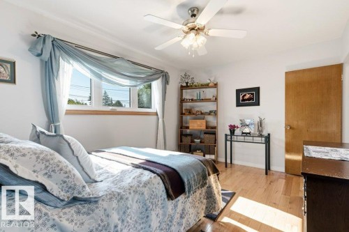 Bright room featuring wood-finish flooring, a multi-pane window with wood trim, a ceiling fan with integrated lighting, and a solid wood door - 10235 74 Street, Edmonton, AB 