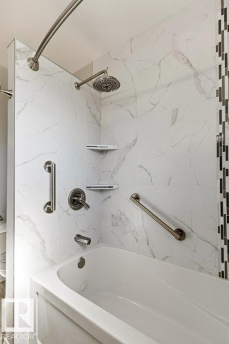 Bathtub-shower combination featuring white marble-look wall tiling with a vertical mosaic accent - 10235 74 Street, Edmonton, AB 