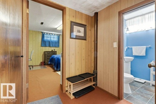 Interior hallway featuring wood paneling, a ceiling-mounted light fixture, and carpet flooring - 10235 74 Street, Edmonton, AB 