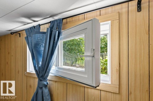 Wood-paneled interior wall with a white casement window open to exterior greenery - 10235 74 Street, Edmonton, AB 