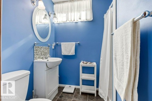 Bathroom featuring a white toilet, pedestal sink with cabinet storage, mosaic tile backsplash, and an oval wall mirror - 10235 74 Street, Edmonton, AB 