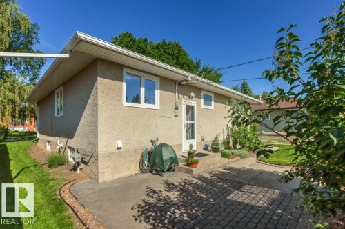 Exterior stucco siding with white trim windows and a white screen door - 10235 74 Street, Edmonton, AB 