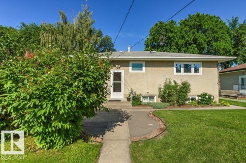 Stucco exterior featuring multiple windows and a white entry door - 10235 74 Street, Edmonton, AB 