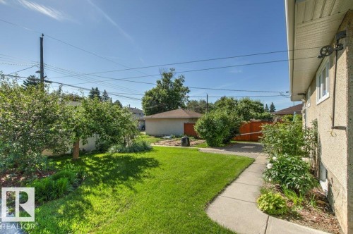 Expansive backyard featuring a lush lawn, mature trees, concrete pathway, and a detached structure with a pitched roof - 10235 74 Street, Edmonton, AB 