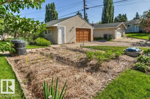 Expansive garden area featuring a mulched bed with small plants, decorative metal edging, and a compost bin - 10235 74 Street, Edmonton, AB 
