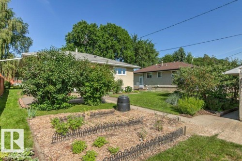 Expansive rear yard featuring a mulched garden bed with decorative edging, a manicured lawn, and mature trees - 10235 74 Street, Edmonton, AB 