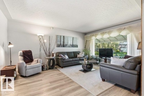 Expansive living area featuring light wood-finish flooring, a large bay window with drapery, and a textured ceiling - 10235 74 Street, Edmonton, AB 