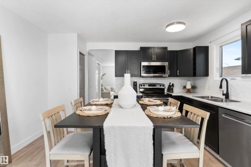Modern kitchen featuring dark cabinetry, stainless steel appliances, white subway tile backsplash, white countertops, and wood-finish flooring - 15252 81 Street, Edmonton, AB 
