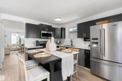 Modern kitchen featuring dark cabinetry with gold-tone hardware, white countertops, a white subway tile backsplash, stainless steel appliances, and wood-finish flooring - 