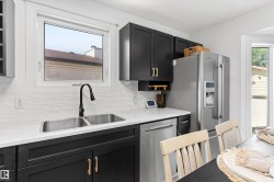 Modern kitchen featuring black cabinetry, light countertops, a stainless steel double-basin sink with a matte black faucet, a white subway tile backsplash, and stainless steel appliances - 