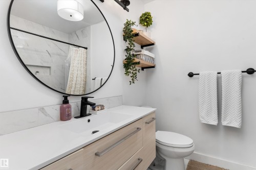 Bathroom vanity featuring a light wood-finish cabinet with modern pulls, a white countertop, and a black-framed round mirror - 15252 81 Street, Edmonton, AB 