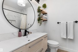 Bathroom vanity featuring a light wood-finish cabinet with modern pulls, a white countertop, and a black-framed round mirror - 