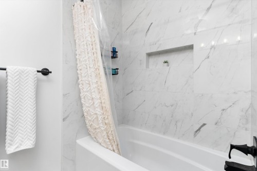 Bathtub with white porcelain tiling featuring grey veining, a built-in shower niche, and matte black fixtures - 15252 81 Street, Edmonton, AB 