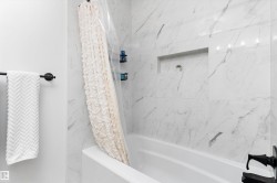Bathtub with white porcelain tiling featuring grey veining, a built-in shower niche, and matte black fixtures - 