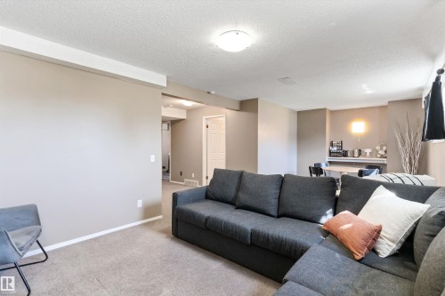 Carpeted recreation room with neutral-toned walls, recessed lighting, and a partial view of a dining area with wall sconce - 15252 81 Street, Edmonton, AB 
