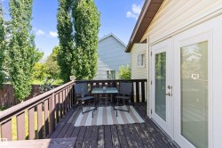 Spacious outdoor deck featuring dark wood-finish flooring, a wood railing, and white double French doors - 