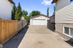 Detached garage with a white overhead door and beige siding, positioned at the rear of a concrete driveway - 
