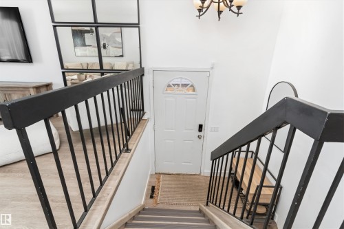 Entryway featuring a white paneled door with an arched transom window, a dark metal chandelier, and a wood-finish staircase with black metal railings - 15252 81 Street, Edmonton, AB 
