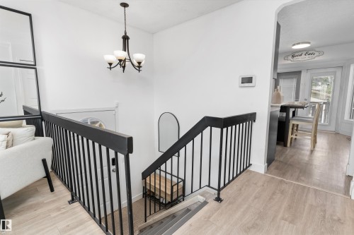 Staircase featuring dark-finished railings and balusters, wood-finish flooring, a wall-mounted light fixture, and an arched entryway to an adjacent room - 15252 81 Street, Edmonton, AB 