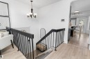Staircase featuring dark-finished railings and balusters, wood-finish flooring, a wall-mounted light fixture, and an arched entryway to an adjacent room - 15252 81 Street, Edmonton, AB 