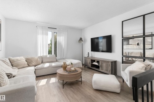 Bright living space featuring wood-finish flooring and a large window with sheer white curtains - 15252 81 Street, Edmonton, AB 