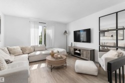 Bright living space featuring wood-finish flooring and a large window with sheer white curtains - 