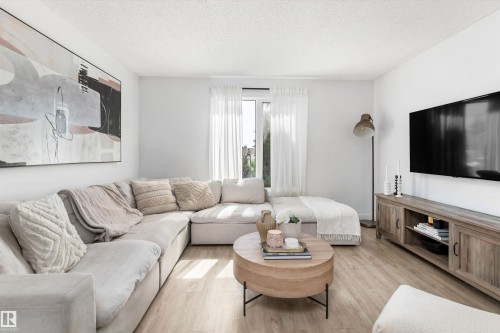 Bright living area featuring wood-finish flooring, white walls, and a large window with sheer drapes - 15252 81 Street, Edmonton, AB 